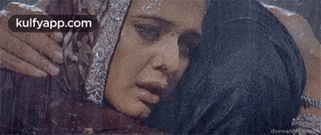 a man is hugging a woman in the rain . the woman is wearing a veil and a nose ring .