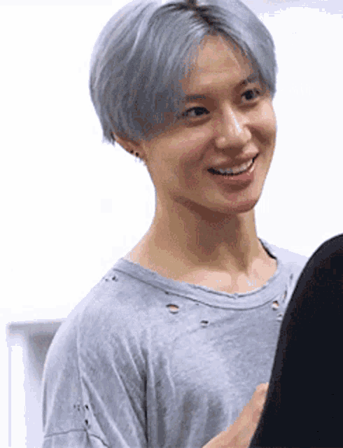 a man with gray hair is smiling and wearing a gray shirt .