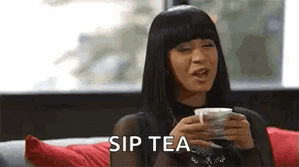 a woman is sitting on a couch holding a cup of tea and saying sip tea .