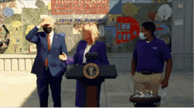 a man in a suit and tie stands behind a podium with a woman in a purple suit behind it