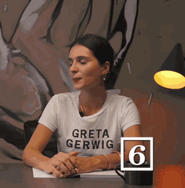 a woman in a greta gerwig shirt sits at a table