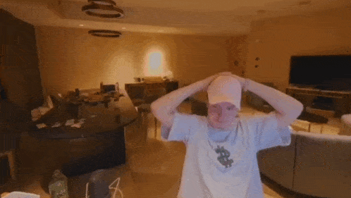 a man wearing a pink hat and a white shirt with a dollar sign on it is standing in a living room .