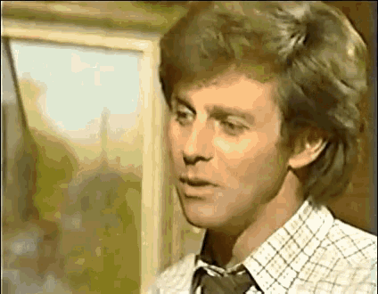 a man in a plaid shirt and tie is standing in front of a window and looking out .
