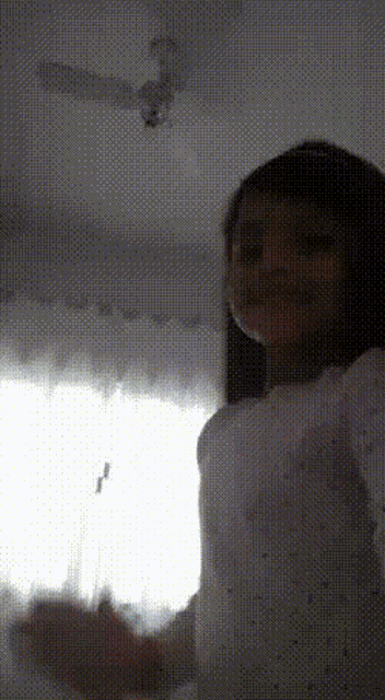a woman standing in front of a window with a ceiling fan in the background
