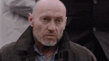 a bald man with a beard wears a black jacket