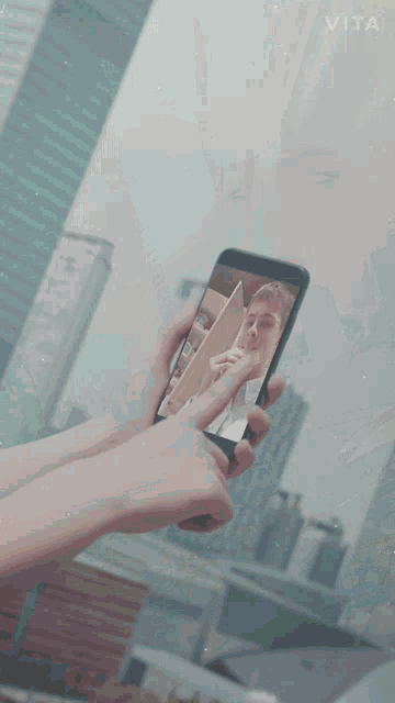 a person holding a cell phone with vita written on the bottom right