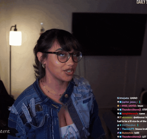 a woman wearing glasses and a denim jacket is sitting in front of a screen that says daily stream