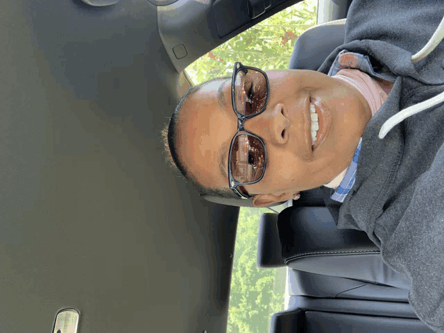 a woman wearing sunglasses is sitting in a car and smiling