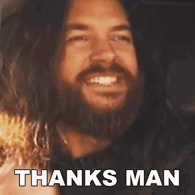 a man with long hair and a beard is smiling with the words thanks man behind him