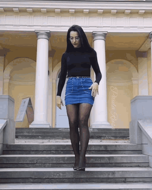 a woman in a black top and blue skirt is standing on a set of stairs with a photo of her taken by paula rose