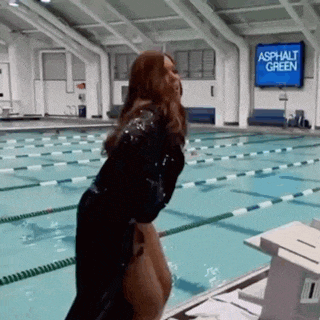 a woman is standing in front of a swimming pool with a sign that says asphalt green on it