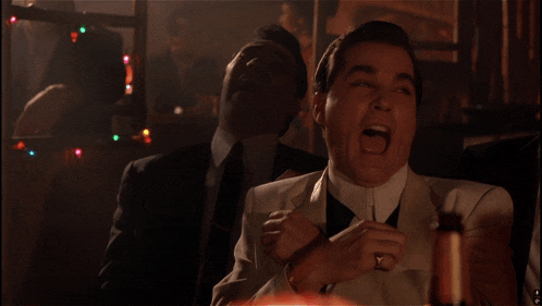 a man in a white suit is laughing with another man in a black suit behind him
