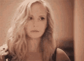 a woman with long blonde hair is looking at the camera in a room .