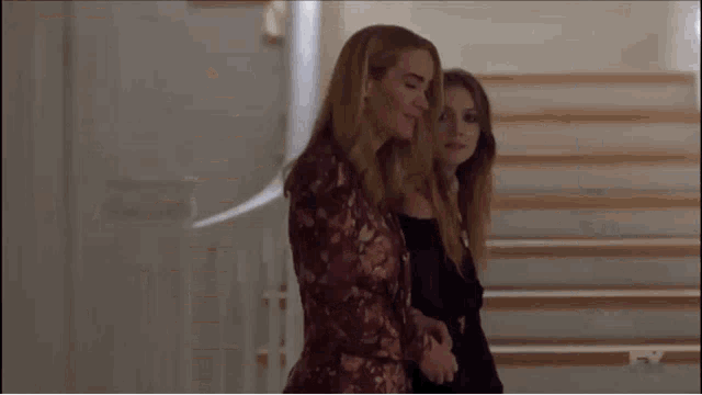 two women are standing next to each other in a room . one of the women is wearing a floral jacket .