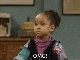 a little girl is sitting at a table making a funny face and saying `` omg '' .