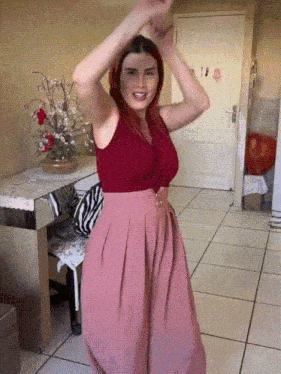 a woman in a red top and pink skirt is dancing in a living room
