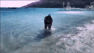 a man in a black shirt is standing in the water near the shore .