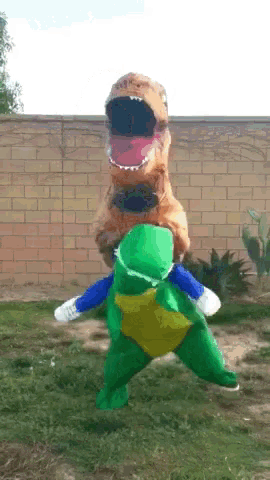 a person in a t-rex costume is carrying another person in a green turtle costume