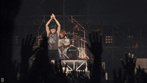 a man stands on a stage in front of a drum set that says sakai