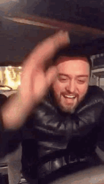 a man with a beard is sitting in the back seat of a car with his hand in the air .