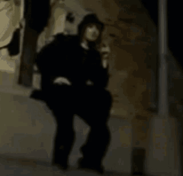a man in a black suit is sitting on a wall talking on a cell phone