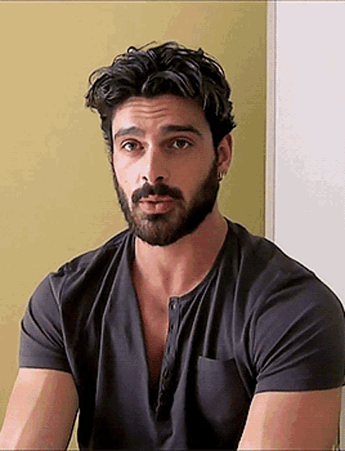 a man with a beard is wearing a grey t-shirt and earrings .
