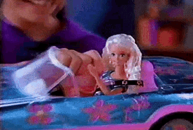 a man is playing with a barbie doll in a pink and blue car .