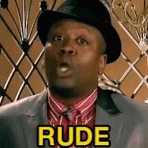 a man in a suit and hat is making a rude gesture .