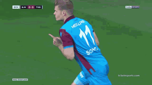 a soccer player in a blue and burgundy shirt holds his finger to his lips