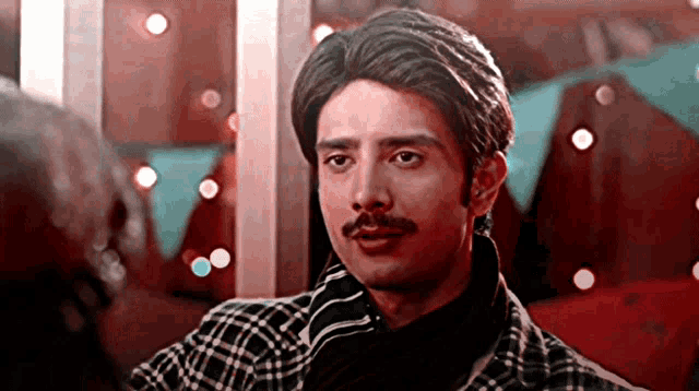 a man with a mustache is wearing a plaid shirt and black shirt