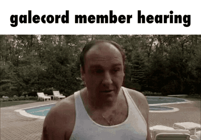 a bald man in a white tank top is standing in front of a pool