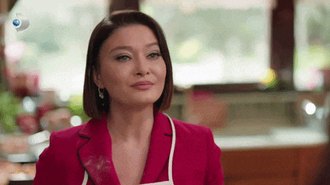 a woman in a red jacket and apron is smiling in a kitchen