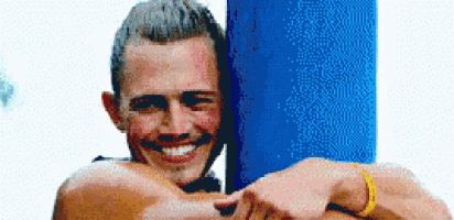 a man with a yellow bracelet on his wrist smiles while standing next to a blue pole