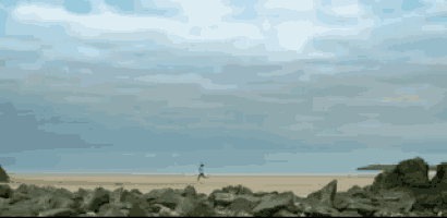 a person is running on a sandy beach with rocks in the foreground