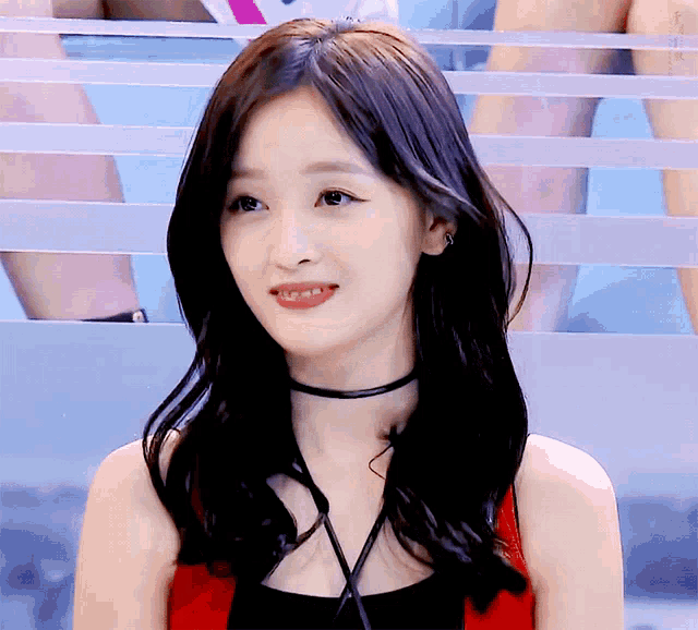a woman wearing a red tank top and a black choker looks at the camera