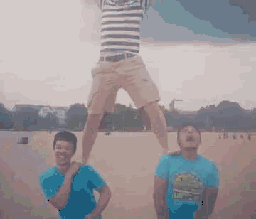 a man in a striped shirt is standing on another man 's shoulders in a field .