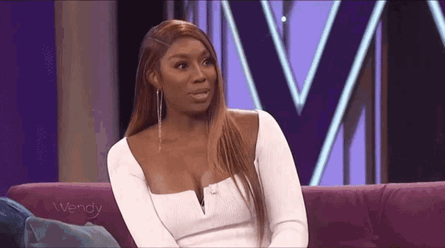 a woman in a white dress is sitting on a purple couch and talking to someone .