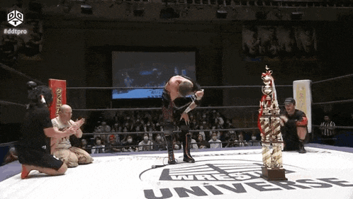 a wrestler is kneeling down in front of a trophy in a wrestling ring in front of a crowd .