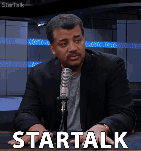 a man in a suit sitting in front of a microphone with the word startalk on the table