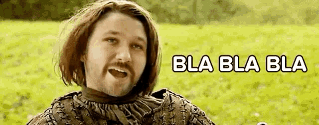 a man with long hair and a beard is standing in a field with the words bla bla bla written above him .