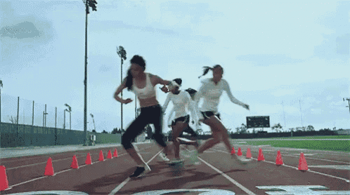 a group of women are running on a track and one of them is wearing a white tank top .