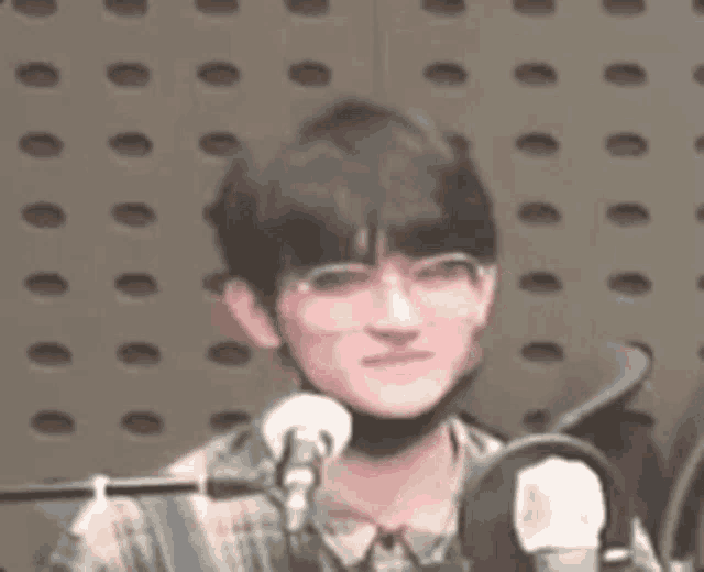 a young man wearing glasses and a mask is sitting in front of a microphone in a recording studio .