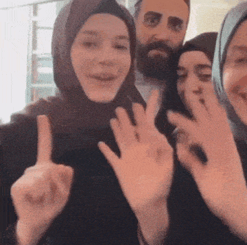 a group of people wearing hijabs are posing for a picture and making signs with their hands .