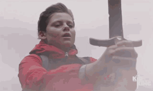 a boy in a red jacket is holding a sword in front of a king logo