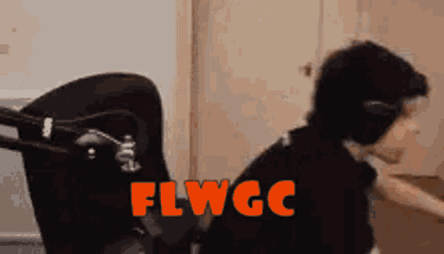 a man wearing headphones is sitting in a chair in front of a microphone with the word flwgc written in orange .