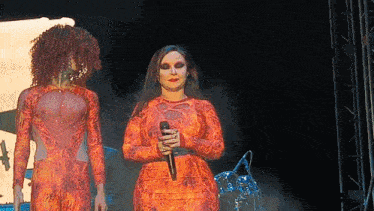 a woman holding a microphone stands next to another woman on stage