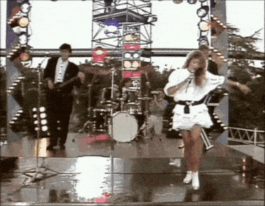 a woman singing into a microphone on a stage with a band