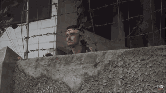 a man with a bandage on his head behind barbed wire