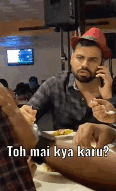 a man wearing a red hat is talking on a cell phone while eating