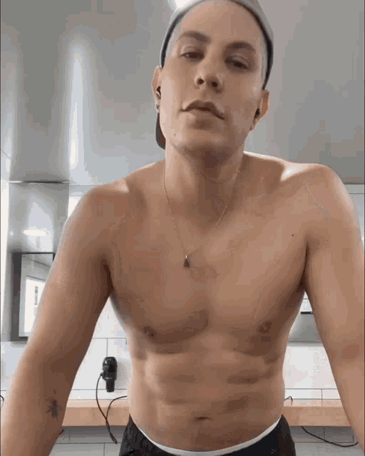 a shirtless man wearing a hat and a necklace is standing in a bathroom